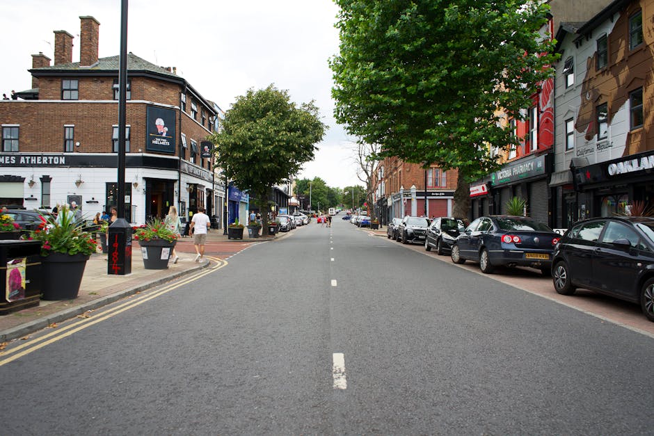 A street scene featuring a row of multi-storey residential buildings with brick facades and gabled roofs, situated along a busy commercial area on High Street Colliers Wood. In the foreground, there a